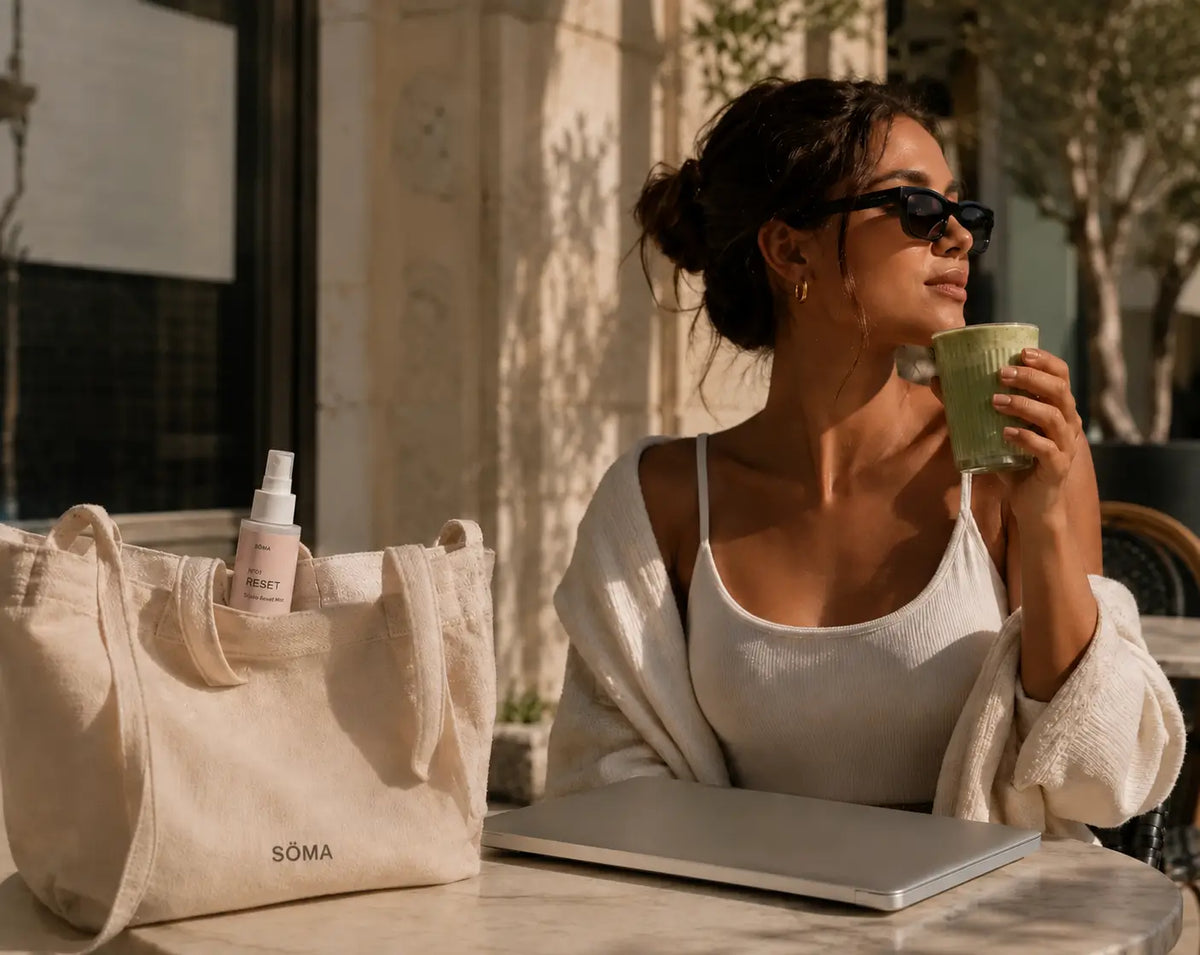 Woman using SÖMA No. 01 Studio Reset Mist as part of her post-Pilates skincare routine while enjoying a matcha at an outdoor café.